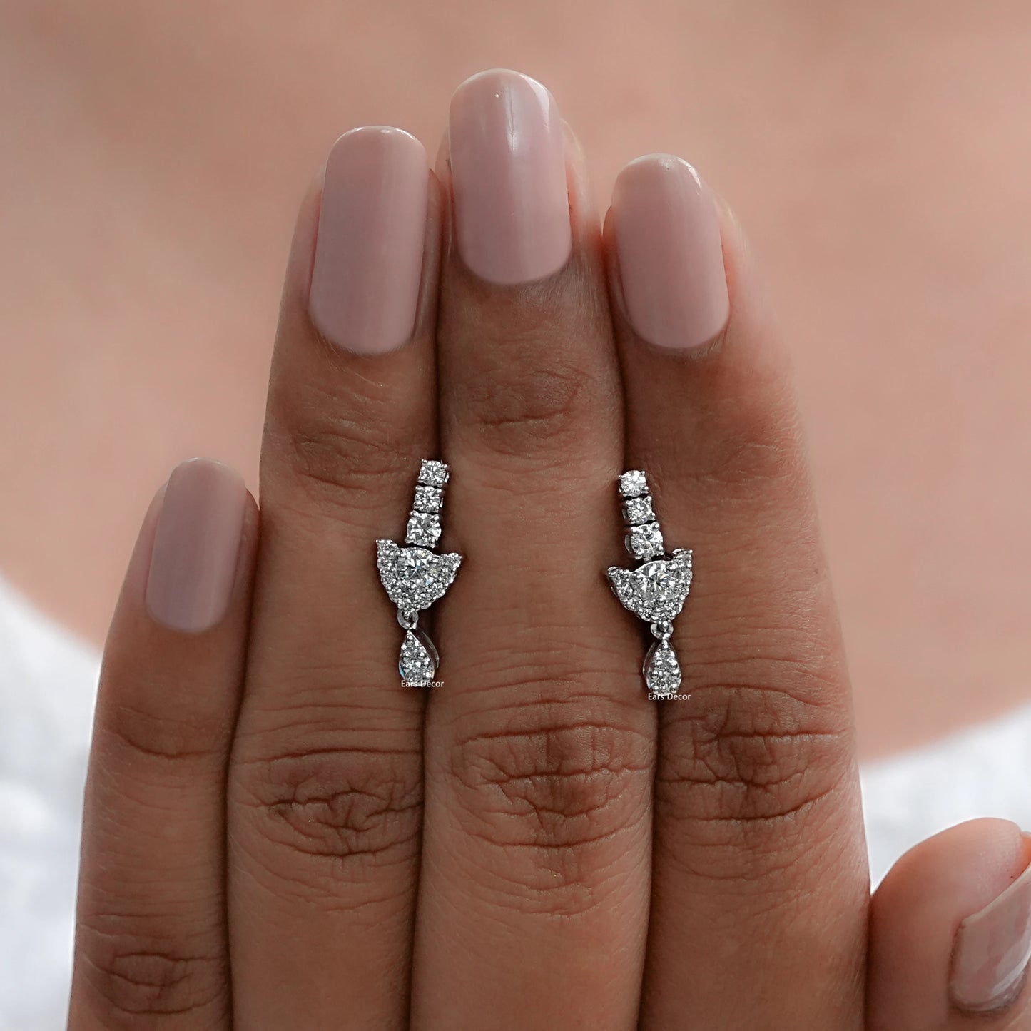 front view of round diamond dangle earrings displayed closely on fingers