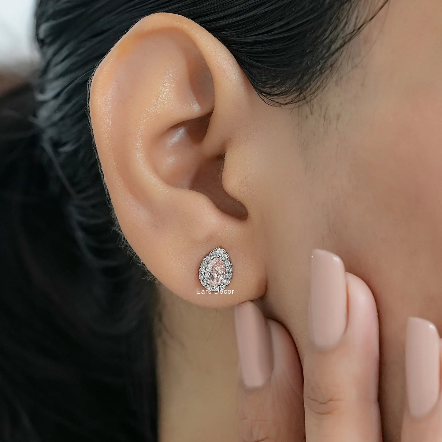 Pink diamond stud earrings with pave halo cluster worn on model ear close-up dark hair nude pink nails hand touching cheek