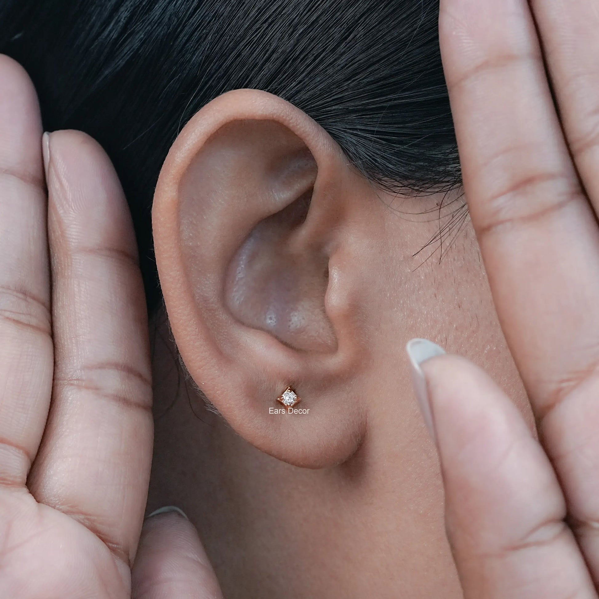 a woman styling a tiny round diamond solitaire stud in her ear