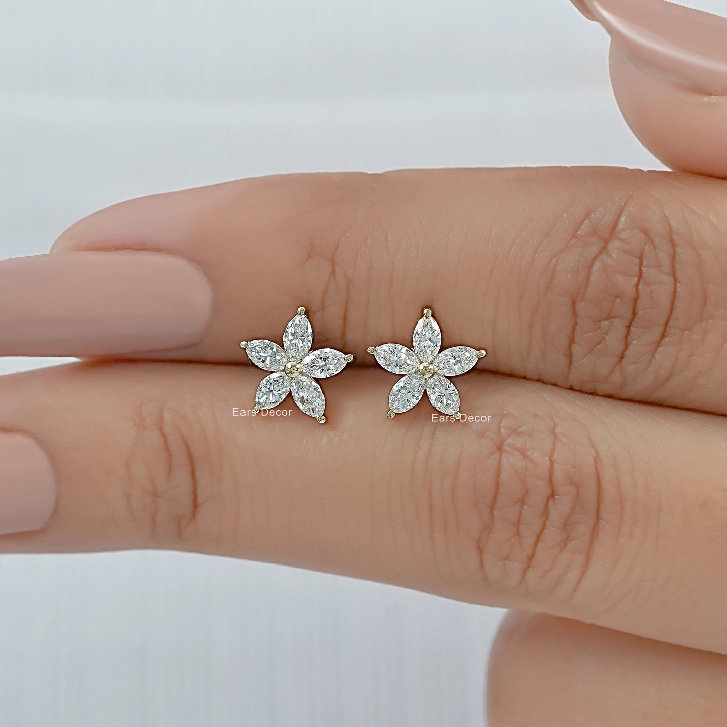 Petite marquise diamond flower earrings in yellow gold held between fingers to show the delicate botanical design.