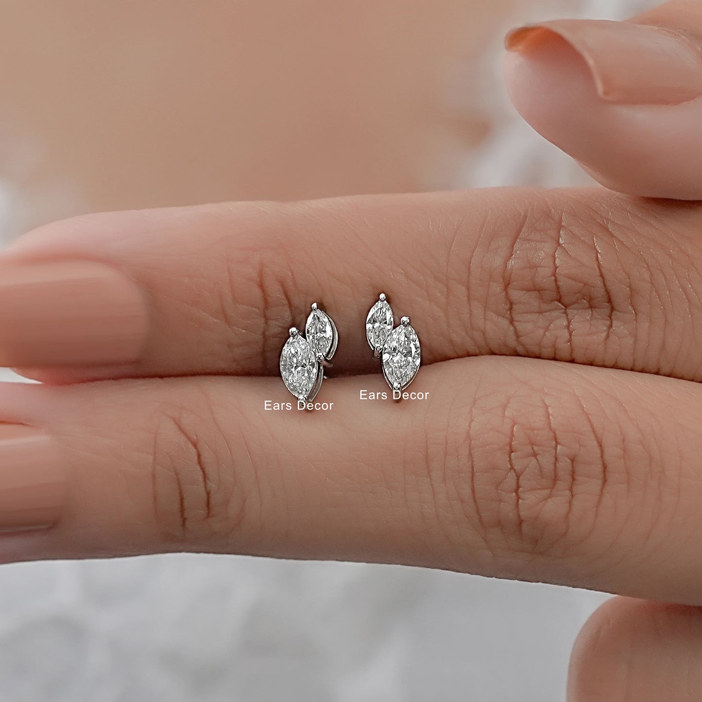 Toi et moi lab diamond stud earrings two marquise stones held between fingers size reference nude pink nails warm skin close-up
