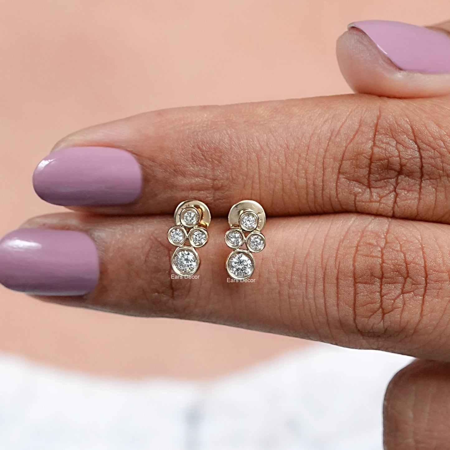 Round lab diamond minimalist stud earrings in gold four diamond bezel cluster resting on palm