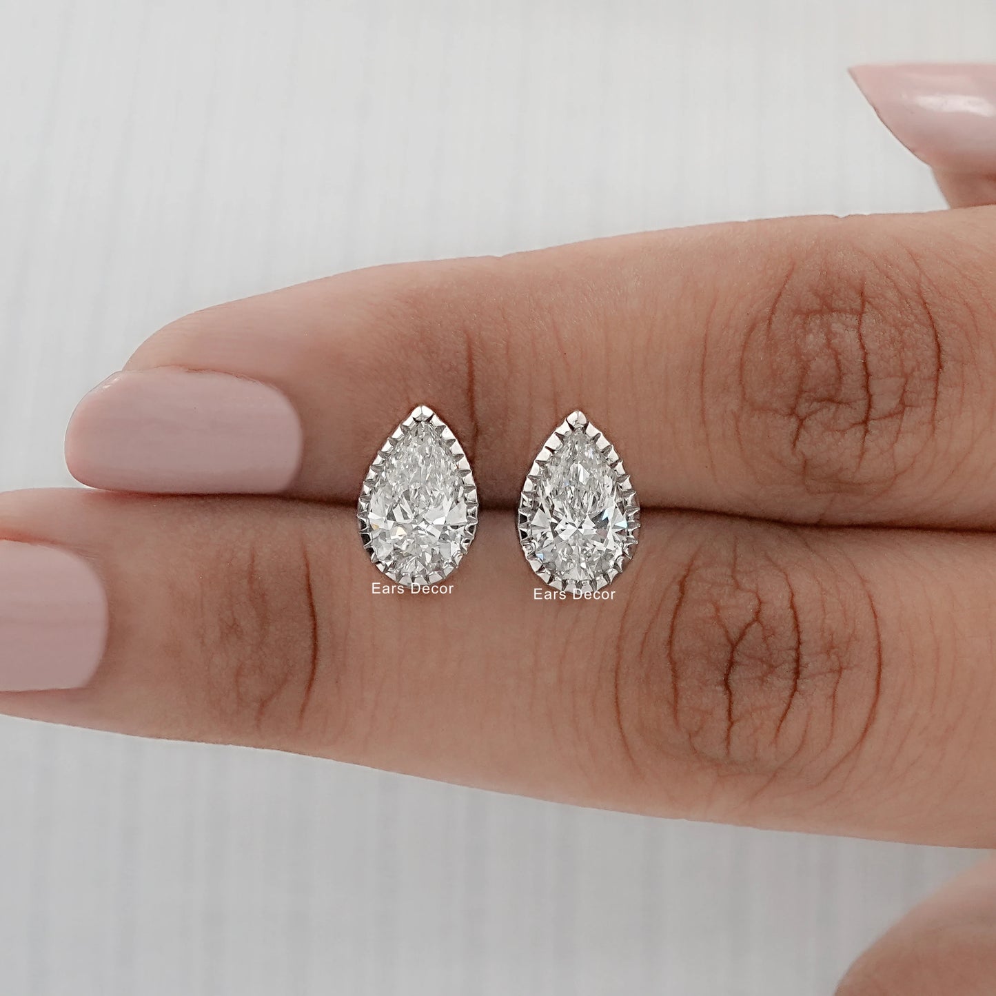pear cut moissanite milgrain stud earrings displayed on fingers showing stone brilliance