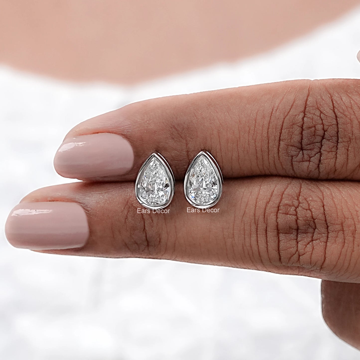 pair of pear shaped moissanite bezel stud earrings displayed on fingers for detail
