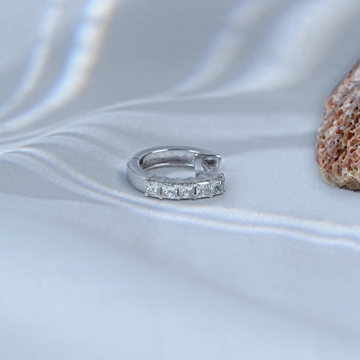 Silver ring with small stones on a textured white surface with a stone in the background