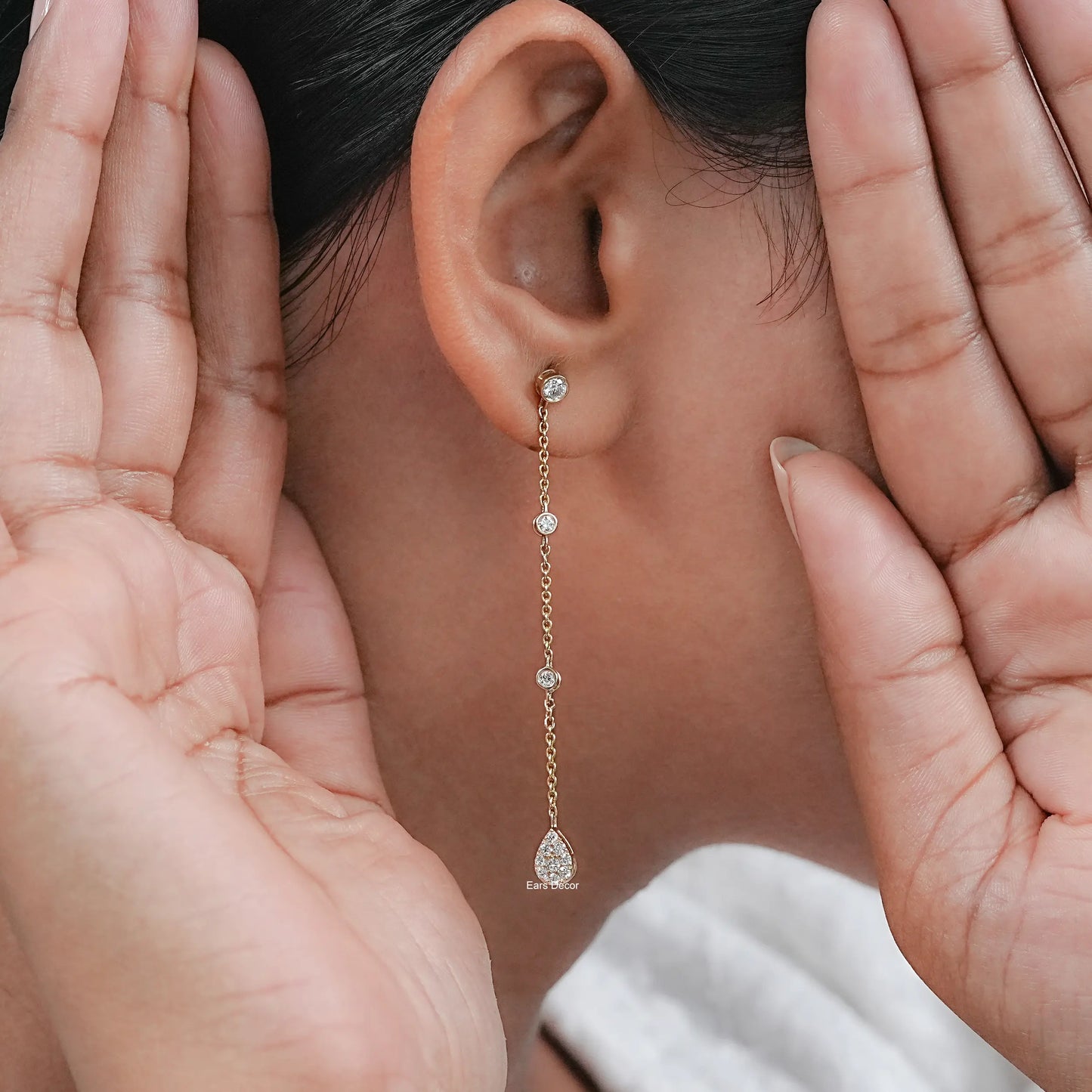 bezel set diamond station drop earring on the ear, highlighted with hands