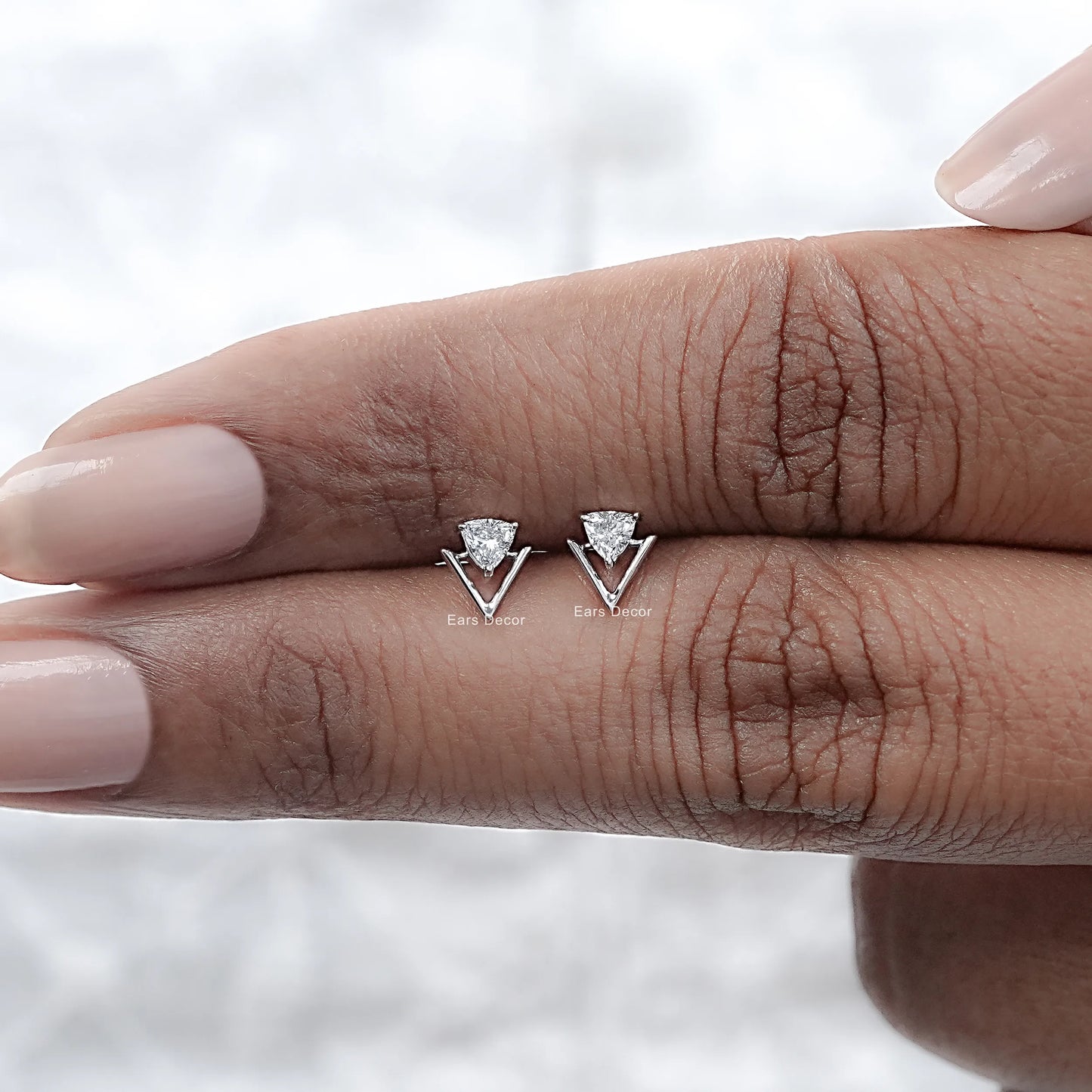 Two dainty silver geometric triangle stud earrings trillion cut brilliant stone open frame displayed on woman knuckles nude manicure closeup