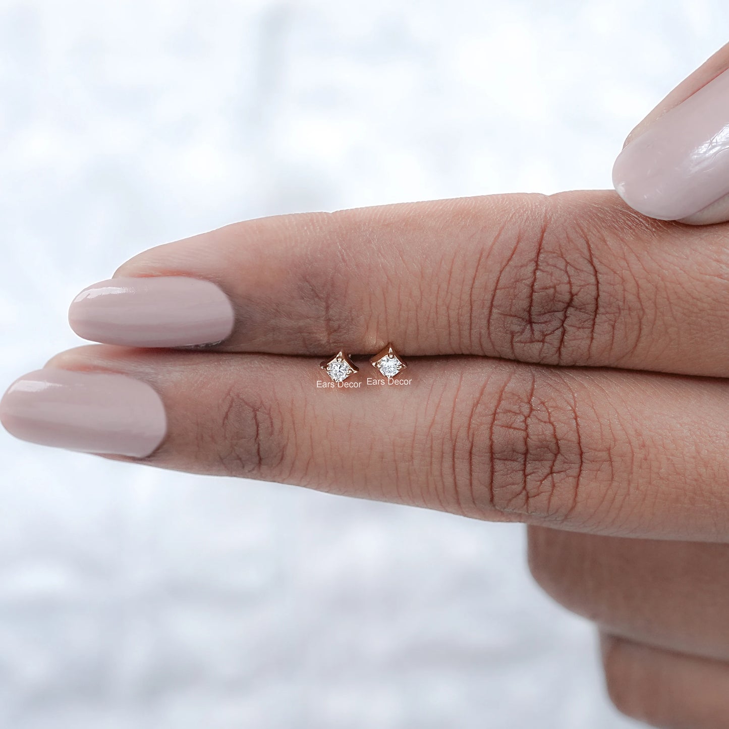 solid gold dainty diamond stud earrings displayed on fingers