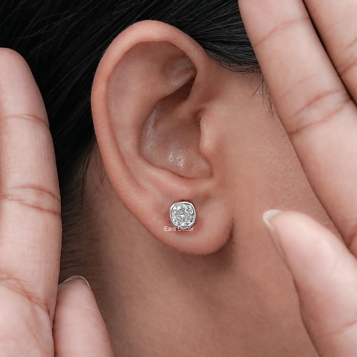 Minimalist cushion cut moissanite diamond stud earring worn on model's ear hands framing