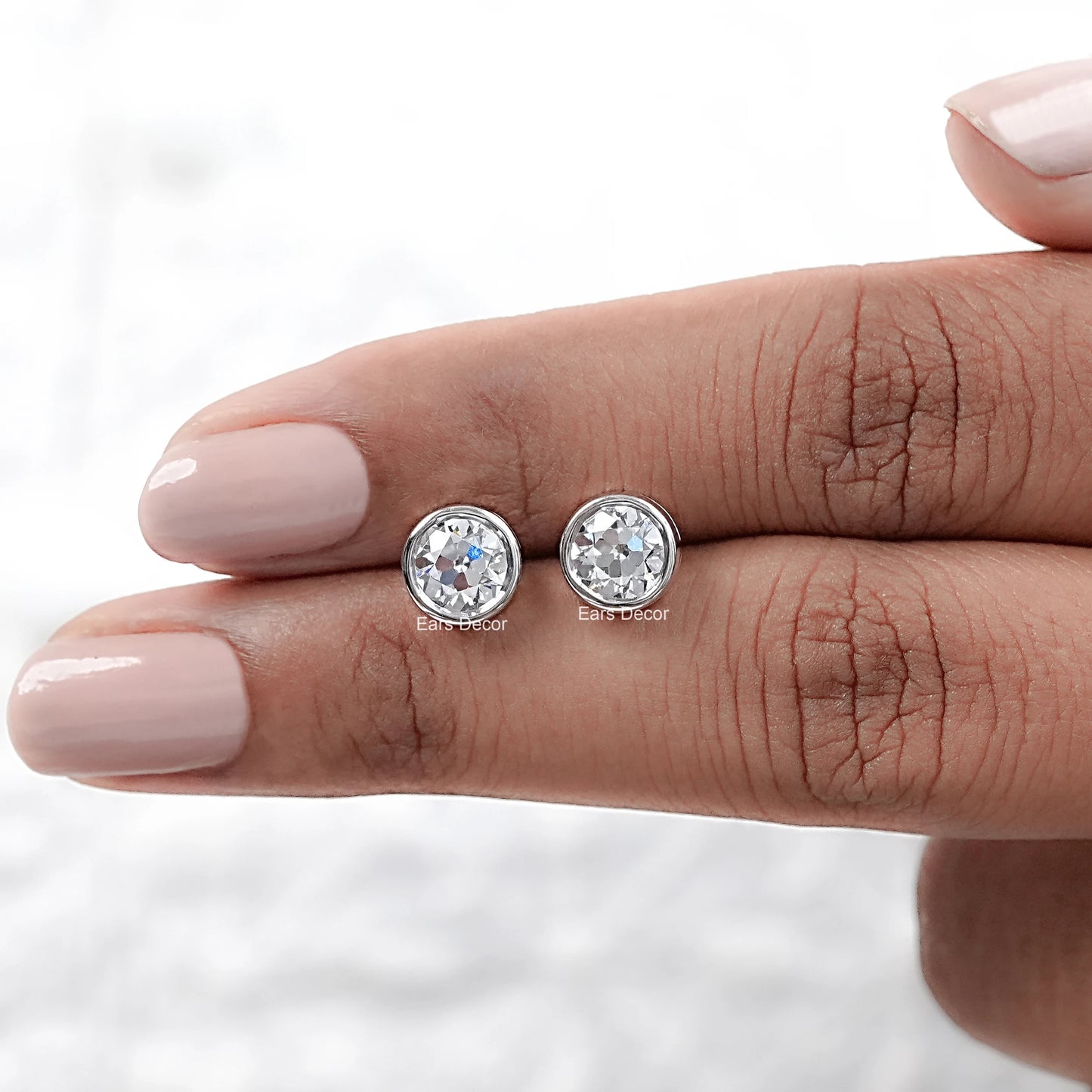 Old European round cut lab diamond bezel set stud earrings displayed on a hand, showcasing their brilliance and design.