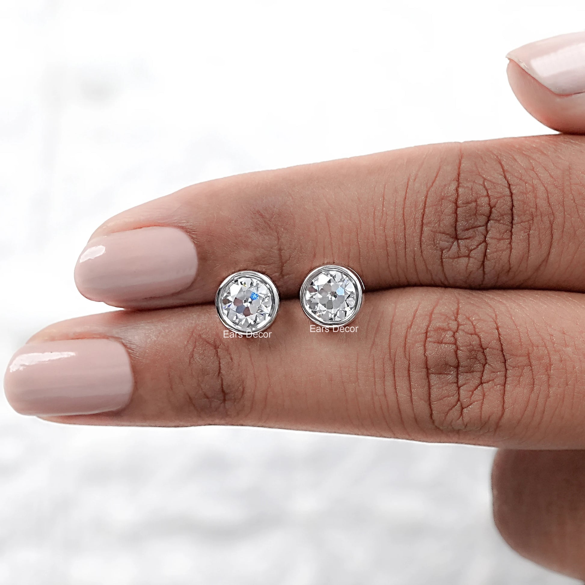 Old European round cut lab diamond bezel set stud earrings displayed on a hand, showcasing their brilliance and design.