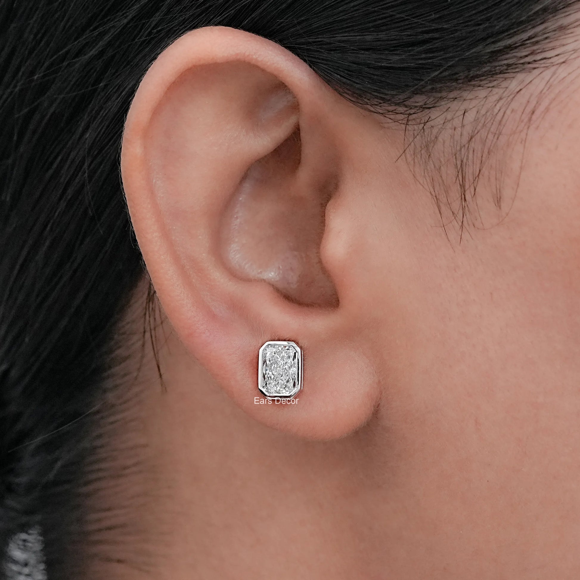 Silver bezel radiant diamond stud earring on model ear close-up, luxury fine jewelry