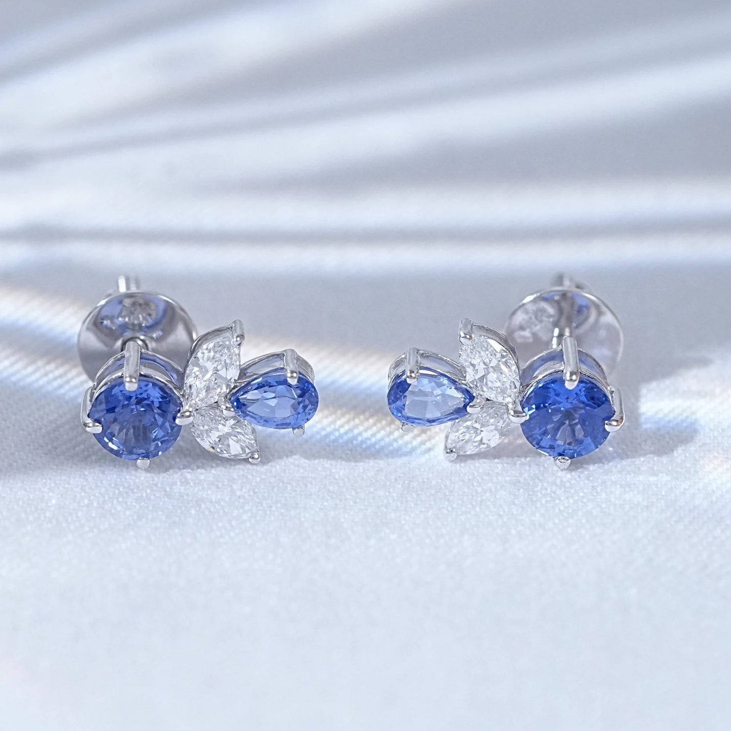 Blue sapphire butterfly stud earrings pair white gold white satin flat lay close-up view
