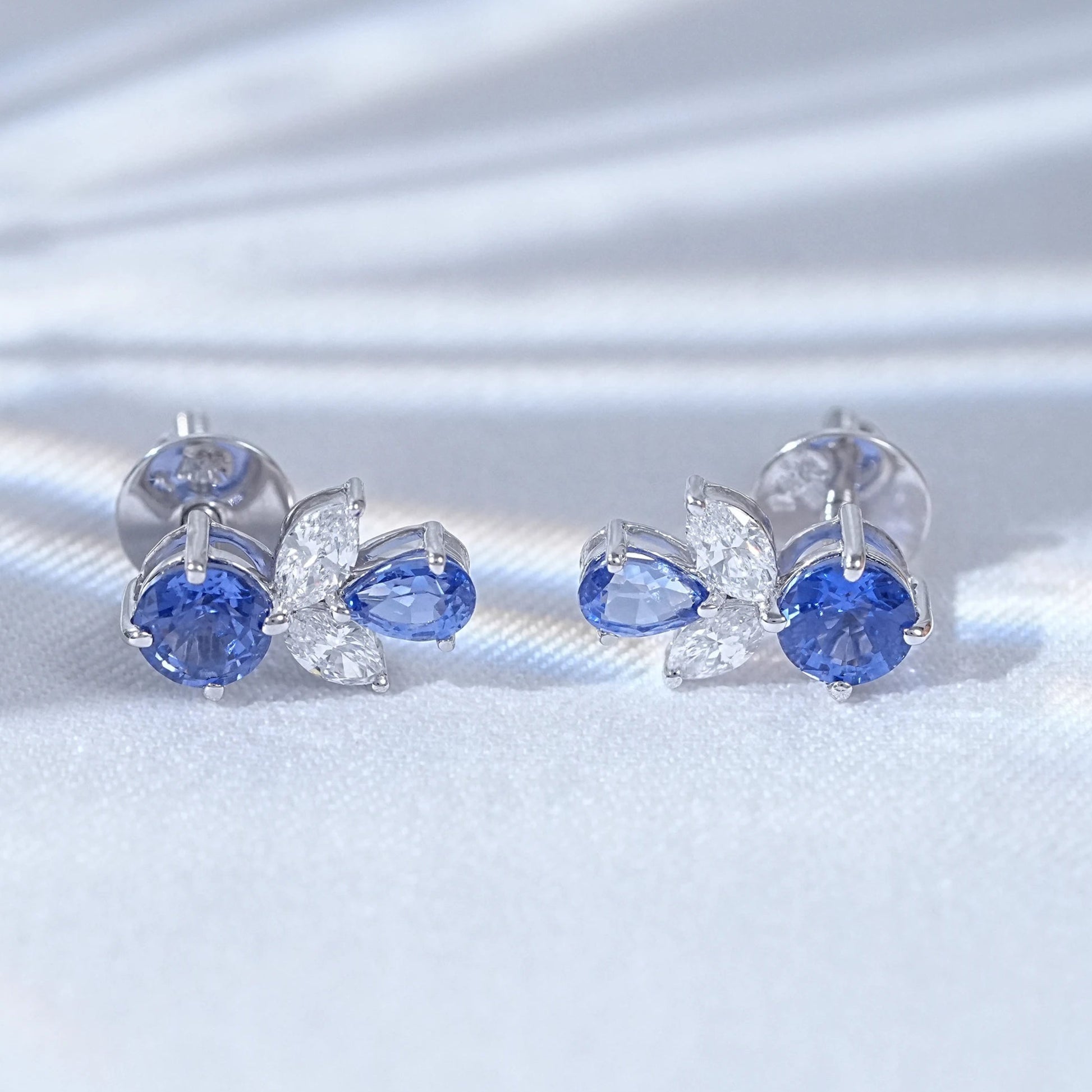 Blue sapphire butterfly stud earrings pair white gold white satin flat lay close-up view