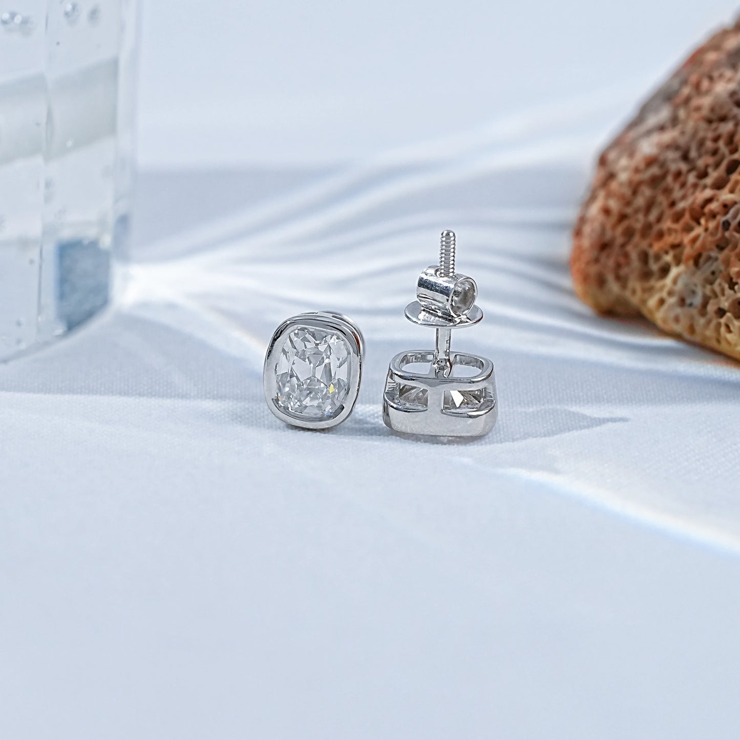 Old Mine Cushion Cut CVD Diamond Stud Earrings in silver setting on white fabric with natural elements.