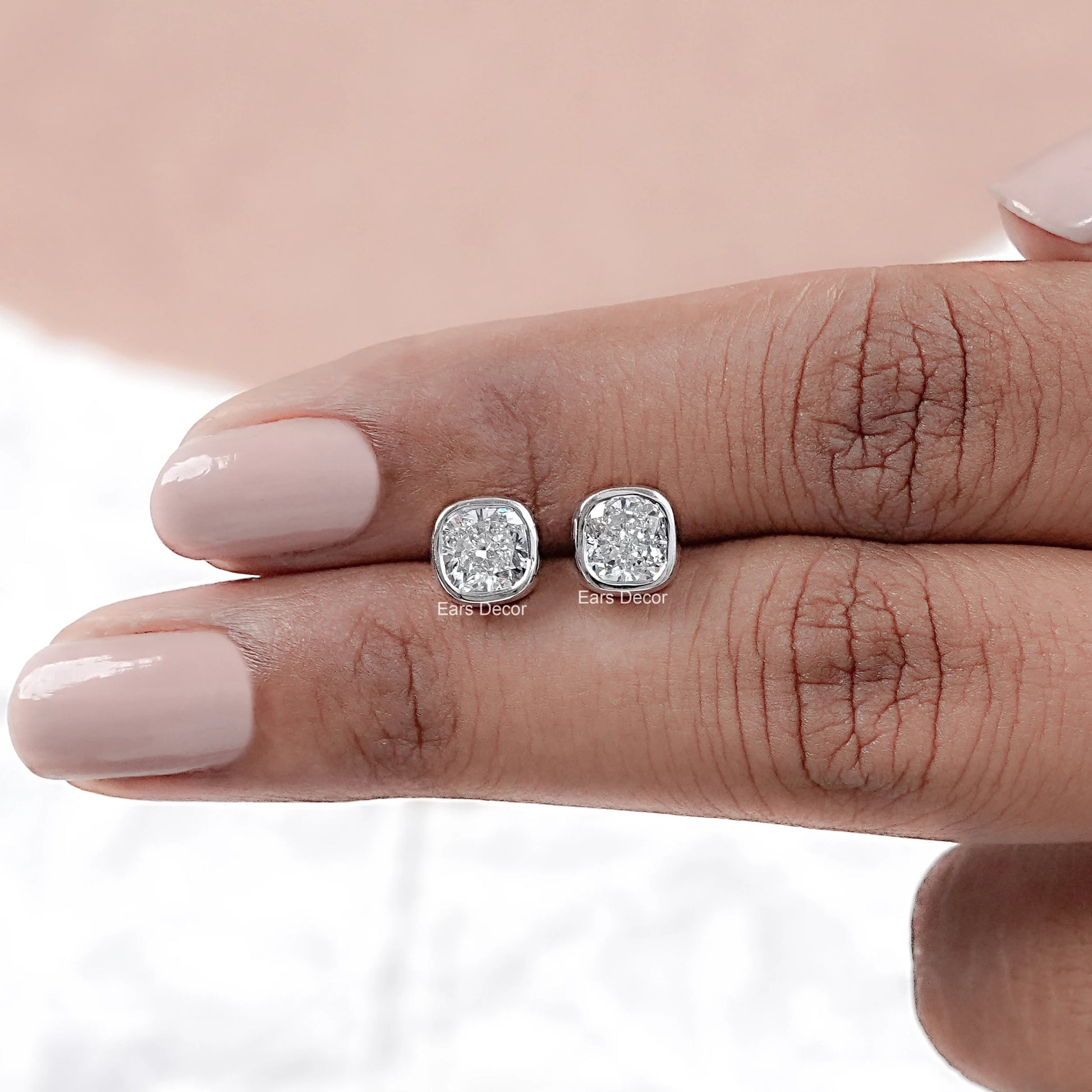 Moissanite diamond solitaire bezel stud earrings pair on model's fingers nude pink nails