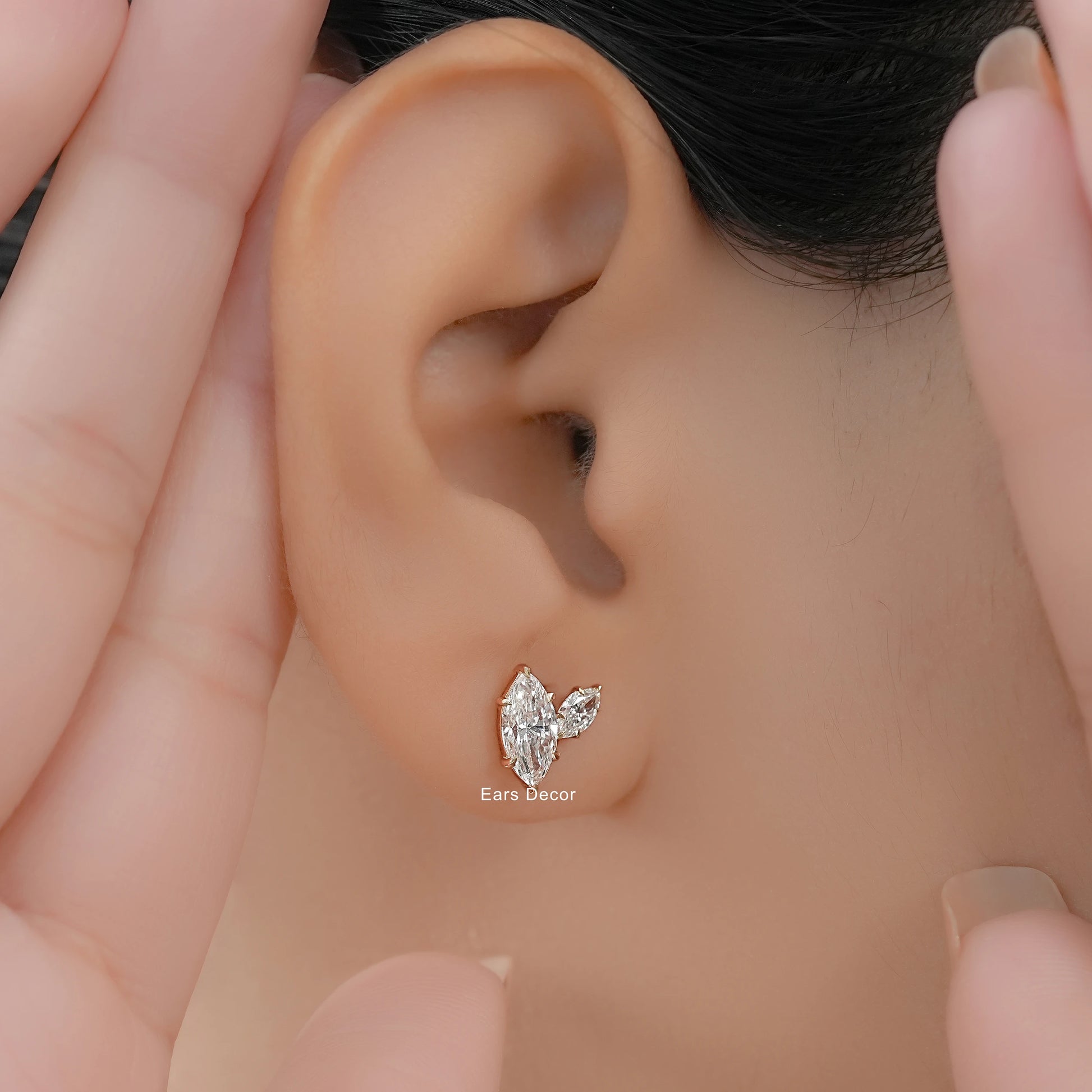 Minimal Toi et Moi diamond earrings with marquise cut stones worn on a model ear framed by hands.