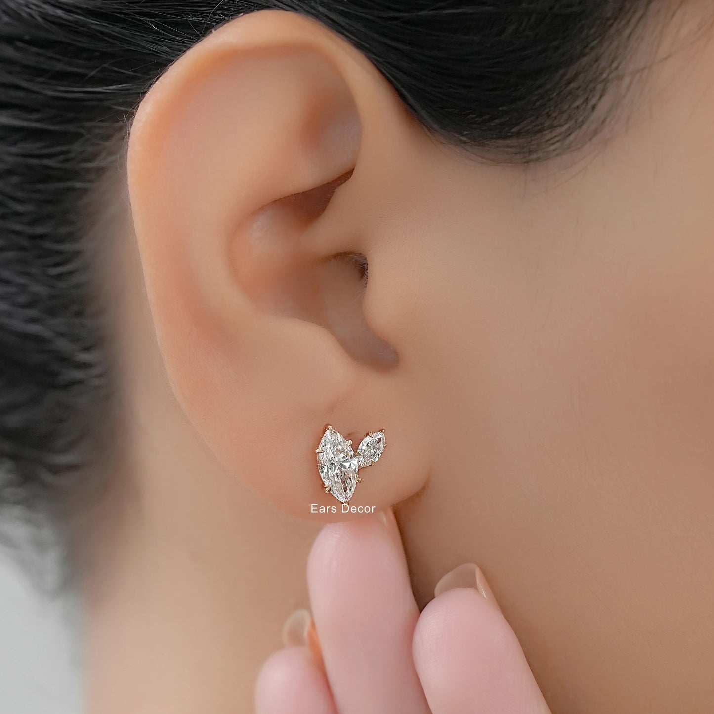 Marquise shape Toi et Moi diamond earrings with side accent stones gold worn on ear close-up soft skin tone