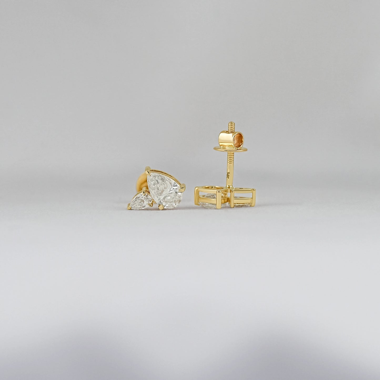 Pear diamond cluster stud earrings gold prong setting front and back view showing yellow gold screw back post clasp detail soft background
