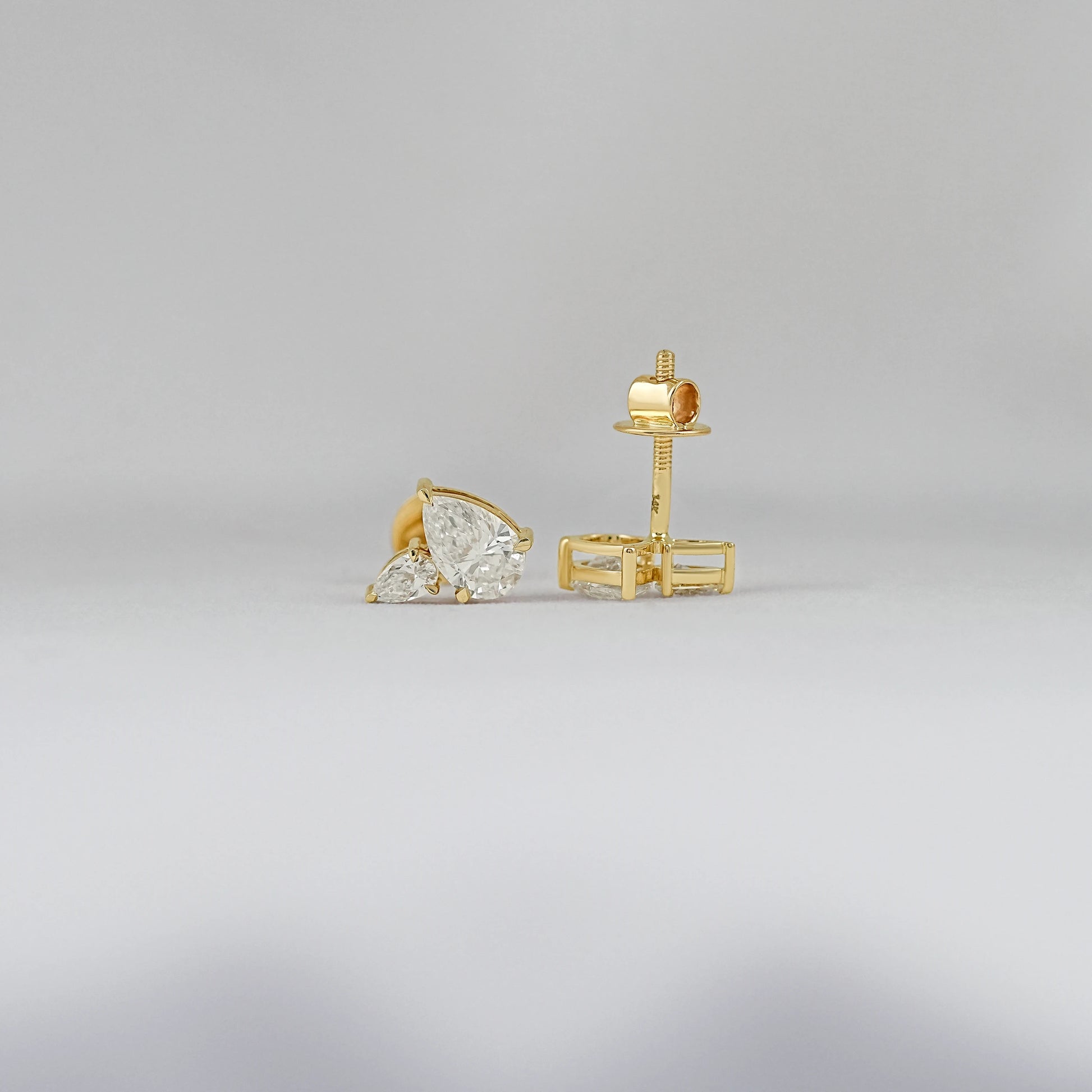 Pear diamond cluster stud earrings gold prong setting front and back view showing yellow gold screw back post clasp detail soft background