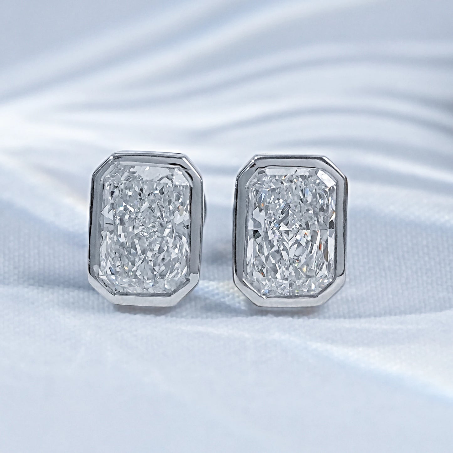 Radiant cut diamond bezel stud earrings pair white gold on satin flatlay close-up