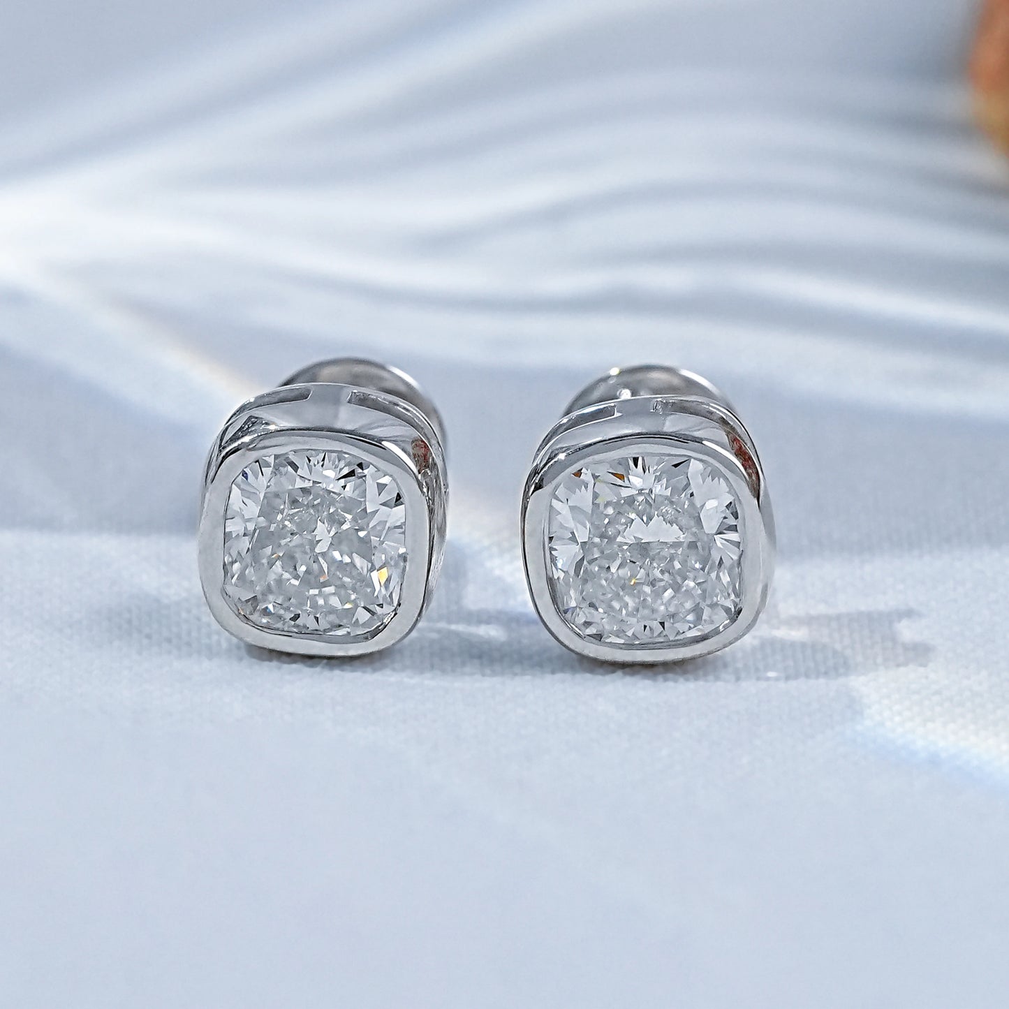Cushion shape bezel diamond studs pair white gold luxury satin flatlay jewelry display