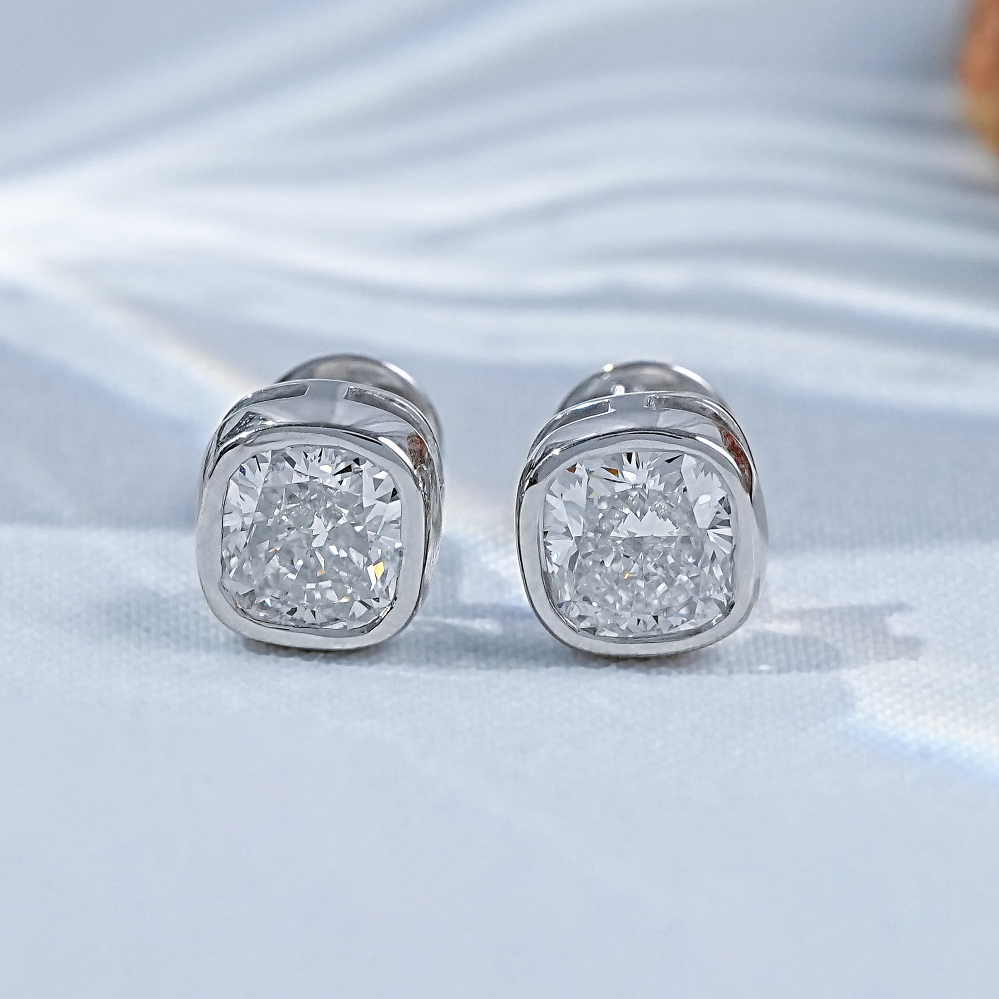 Cushion shape bezel diamond studs pair white gold luxury satin flatlay jewelry display