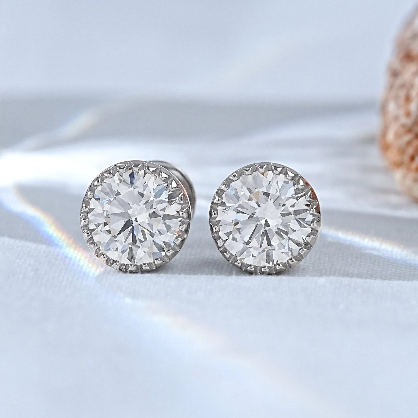 Classic solitaire moissanite stud earrings for women white gold pair on white silk fabric flat lay close-up