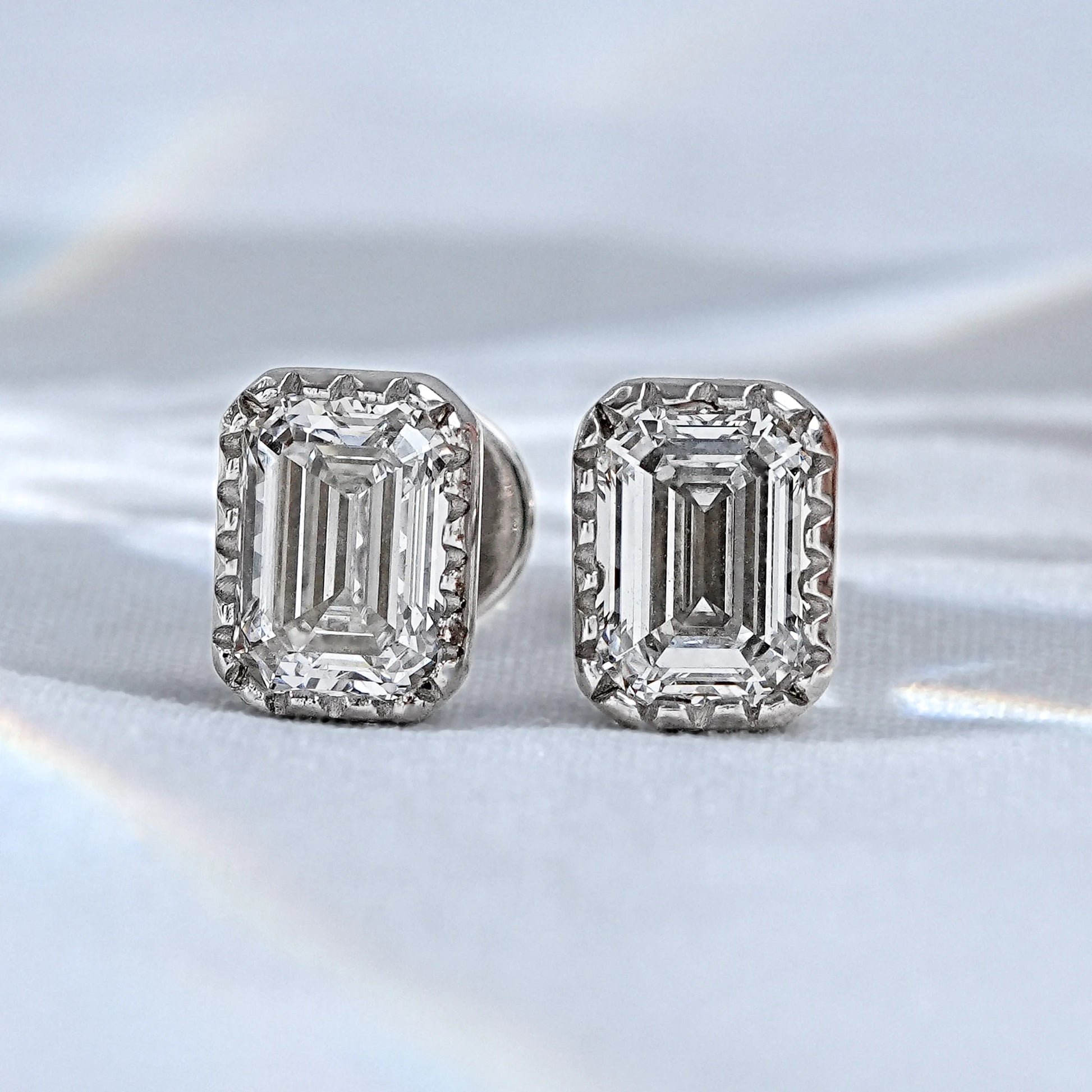 Emerald cut diamond stud earrings pair white gold milgrain bezel satin flatlay close-up