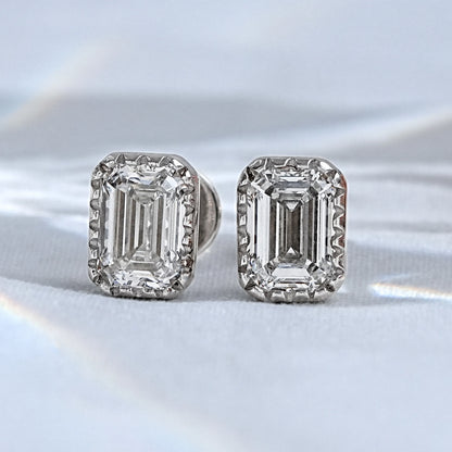 Emerald cut diamond stud earrings pair white gold milgrain bezel satin flatlay close-up