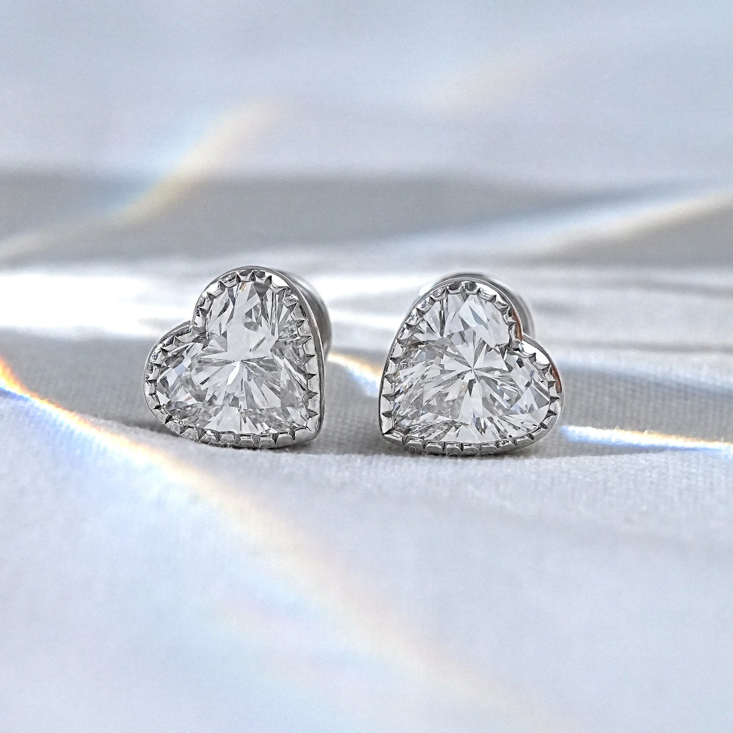 A pair of heart lab diamond earrings resting on fingertips, featuring a delicate beaded milgrain border that adds a vintage inspired charm to the brilliant lab grown diamond.