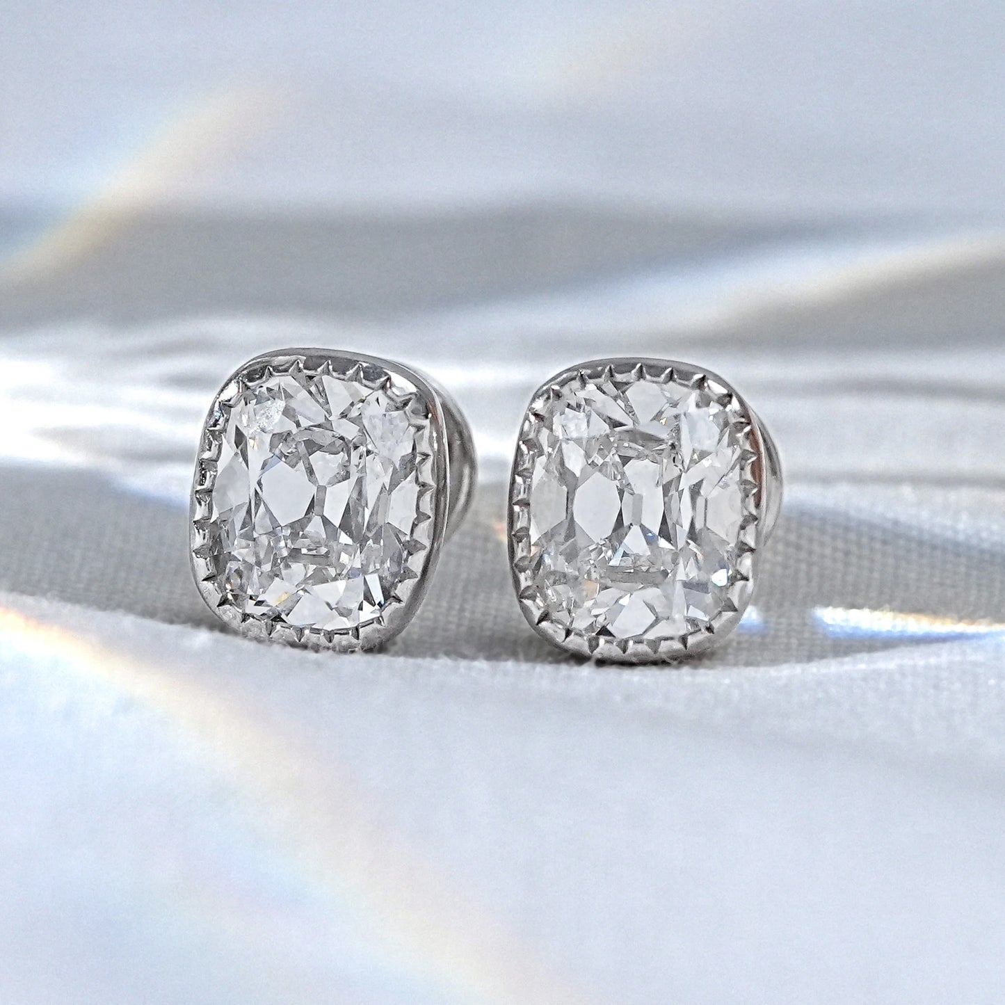 Cushion cut diamond stud earrings white gold milgrain bezel halo setting pair product photo white satin surface soft light
