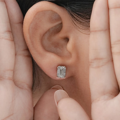 White gold emerald cut diamond studs worn on model's ear, both hands framing close-up