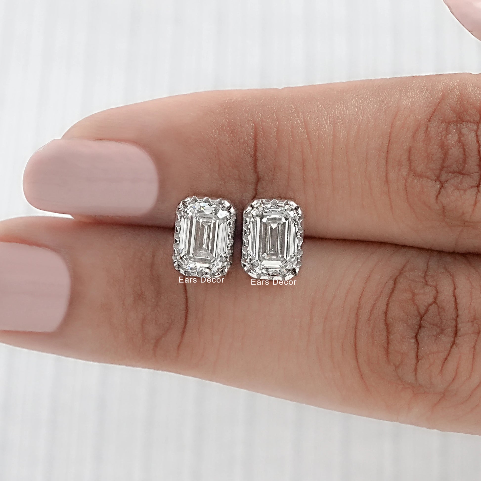Square emerald cut diamond stud earrings pair on model's fingers with nude pink manicure