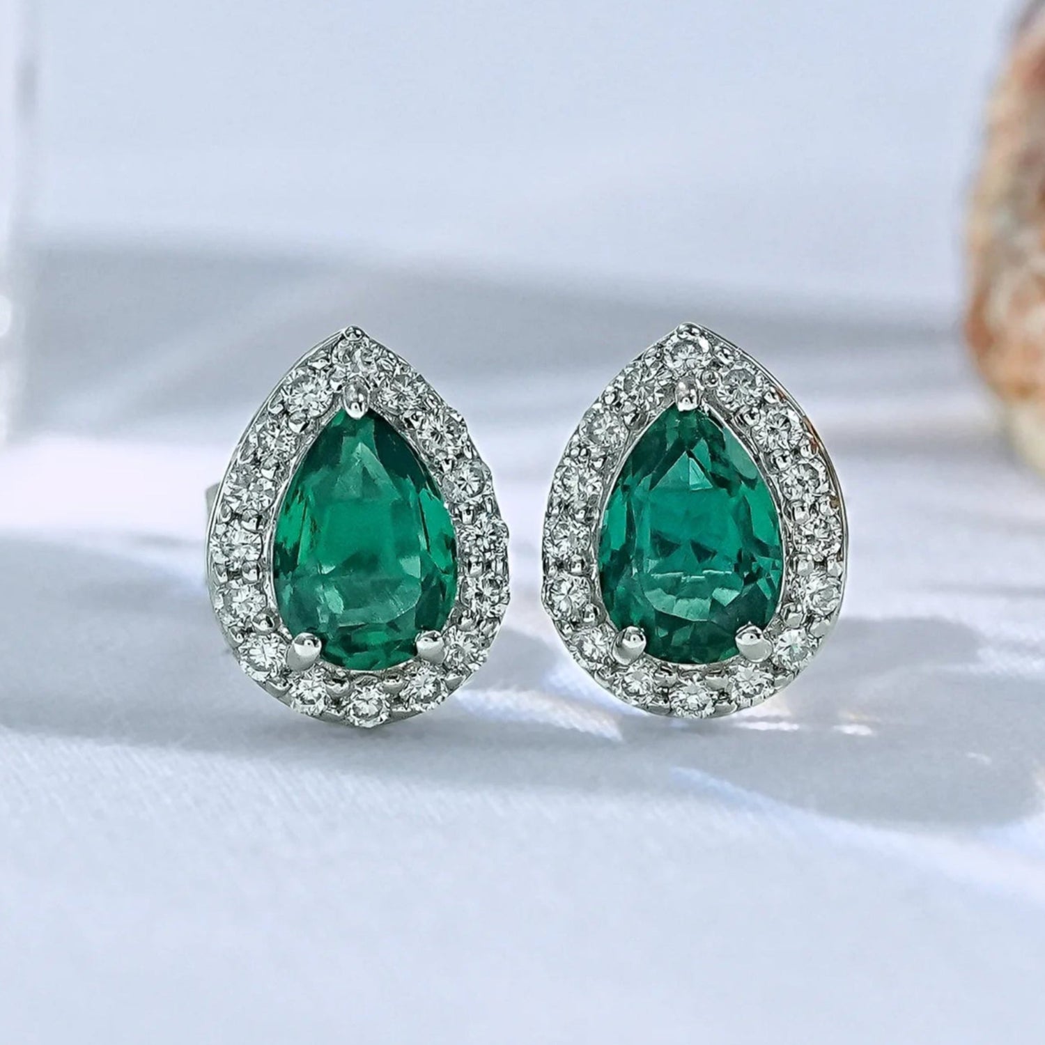 Pear shaped emerald halo stud earrings with sparkling diamond surround in white gold prong setting close-up product shot