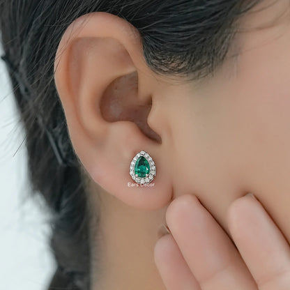 Lab created emerald halo stud earrings with brilliant cut diamond accents worn on model ear close-up dark hair hand touching face