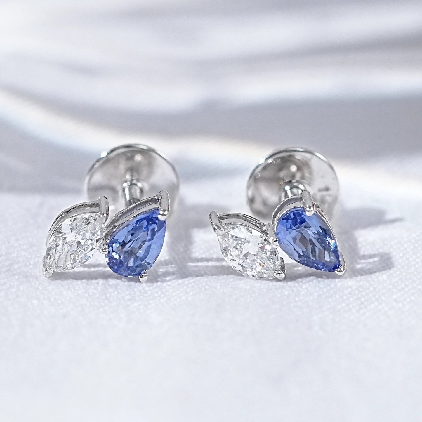 Dainty pear cut sapphire stud earrings diamond leaf design silver white gold blue teardrop clear marquise pair flat lay white linen