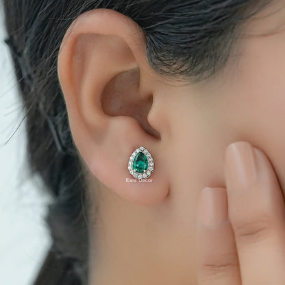 Classic bridal emerald stud earrings with teardrop center stone and diamond halo worn on woman ear side view