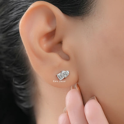Small heart shaped and emerald cut diamond stud earrings women white gold worn on model ear close-up dark hair warm skin nude nails fingers touching
