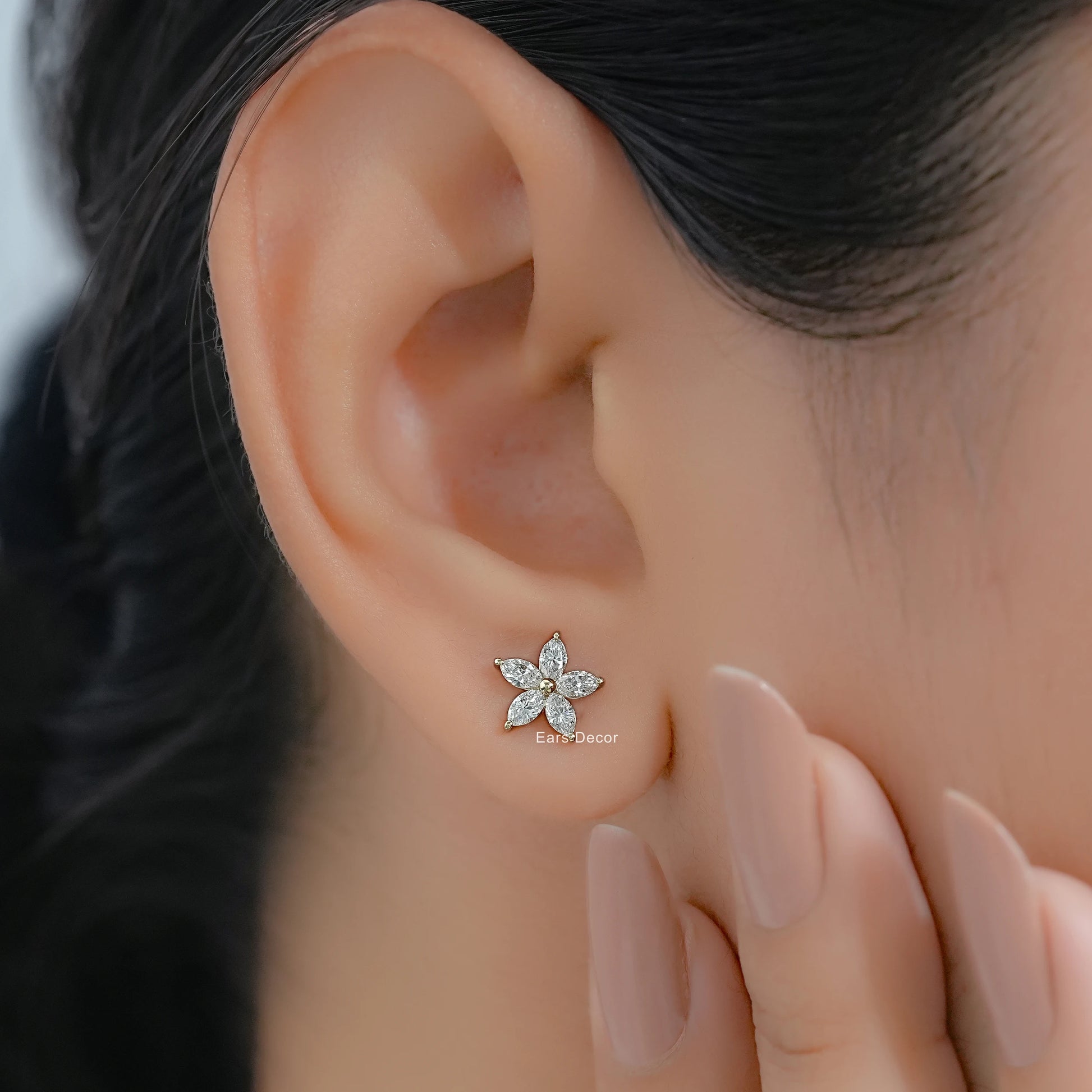 Marquise and pear shape diamond stud earrings on a model with dark hair and nude pink nails.