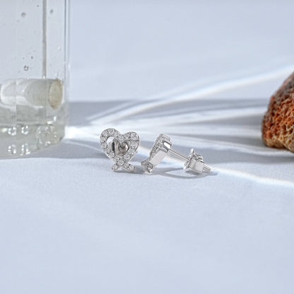 Minimalist heart shaped diamond earrings in white gold displayed on a clean, bright studio surface.