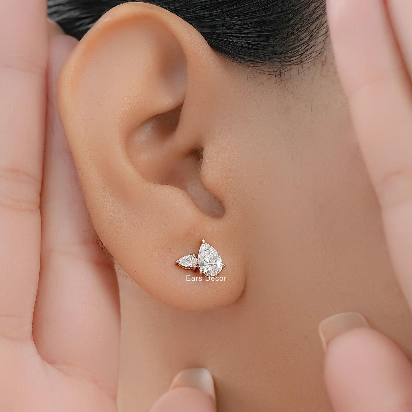 Pear cut diamond cluster design earrings worn on model ear close-up dark hair both hands framing face warm skin gifting jewelry