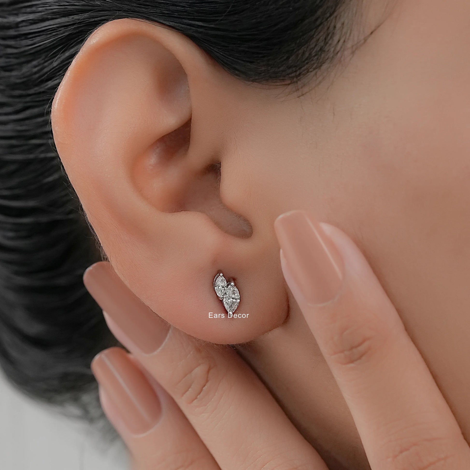 Minimalist white gold toi et moi stud earrings worn on model ear close-up dark hair nude pink nails hand touching cheek warm skin
