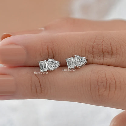 Romantic heart and emerald diamond earrings gift girlfriend wife white gold pair held on warm skin model fingers close-up nude pink nails peach background
