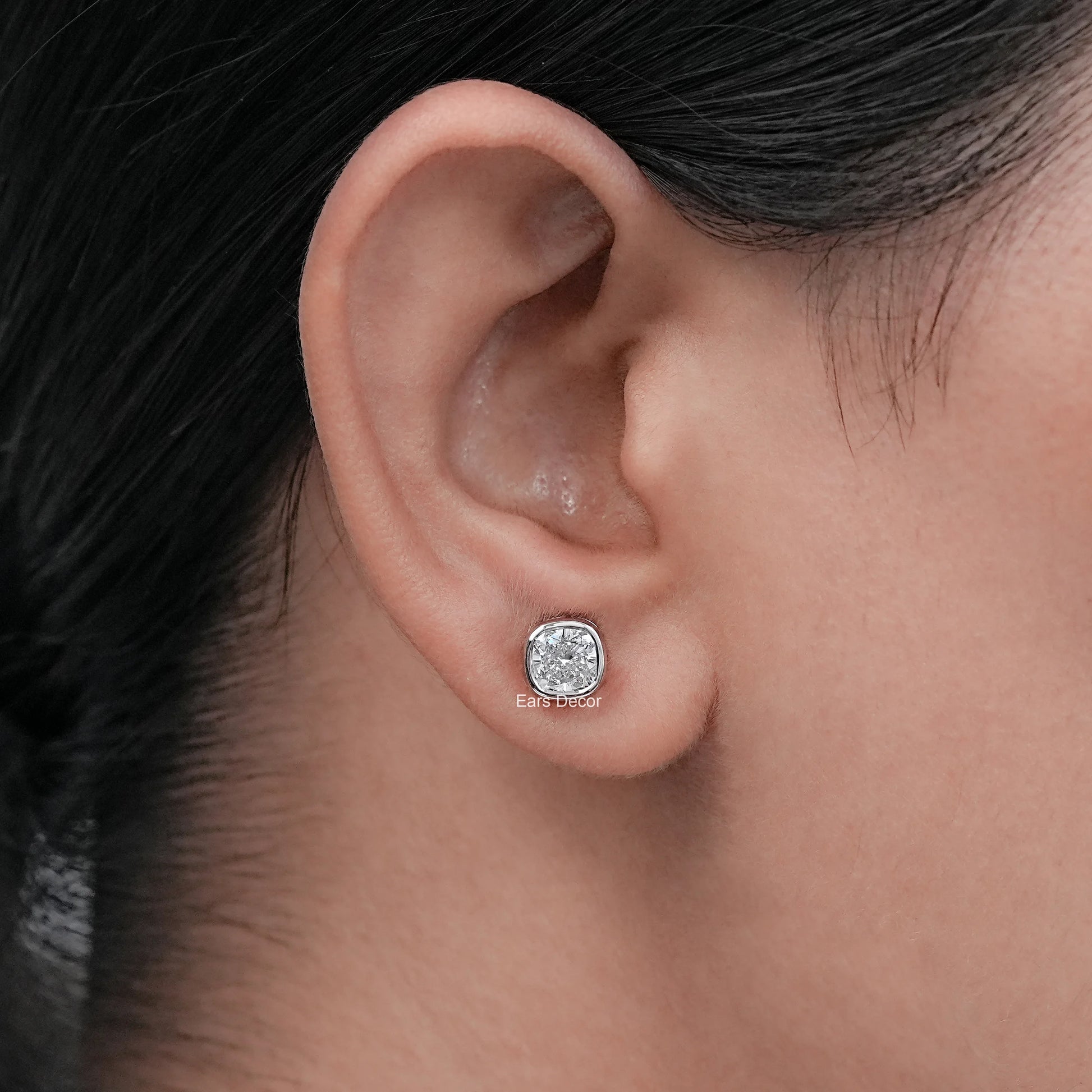Classic cushion bezel diamond studs worn on model's ear, white gold luxury close-up shot