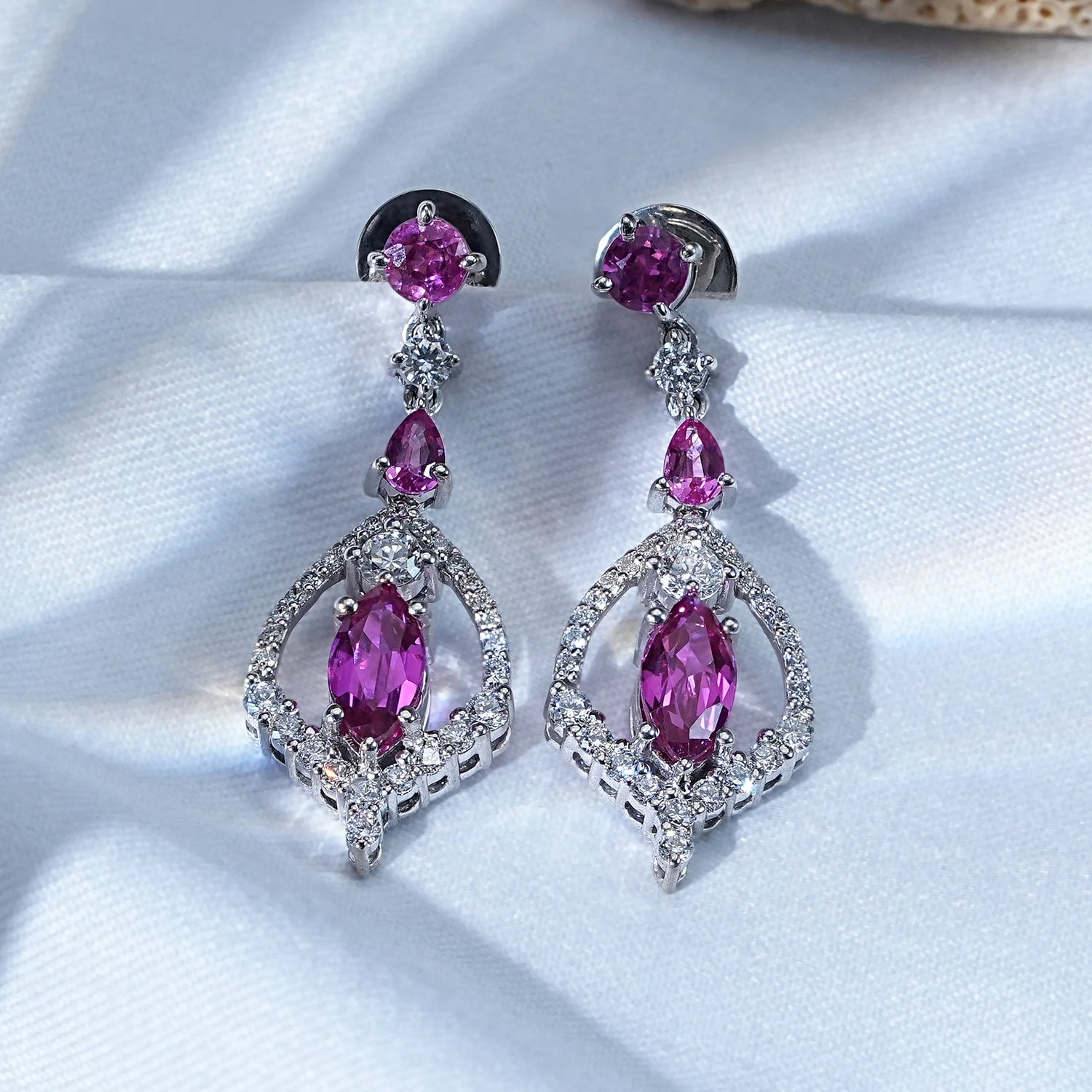 Pink marquise cut gemstone drop earrings with diamonds white gold pair on white silk fabric flat lay