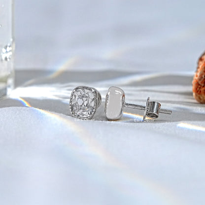 White gold cushion cut diamond studs classic milgrain setting pair displayed white satin side view soft rainbow light