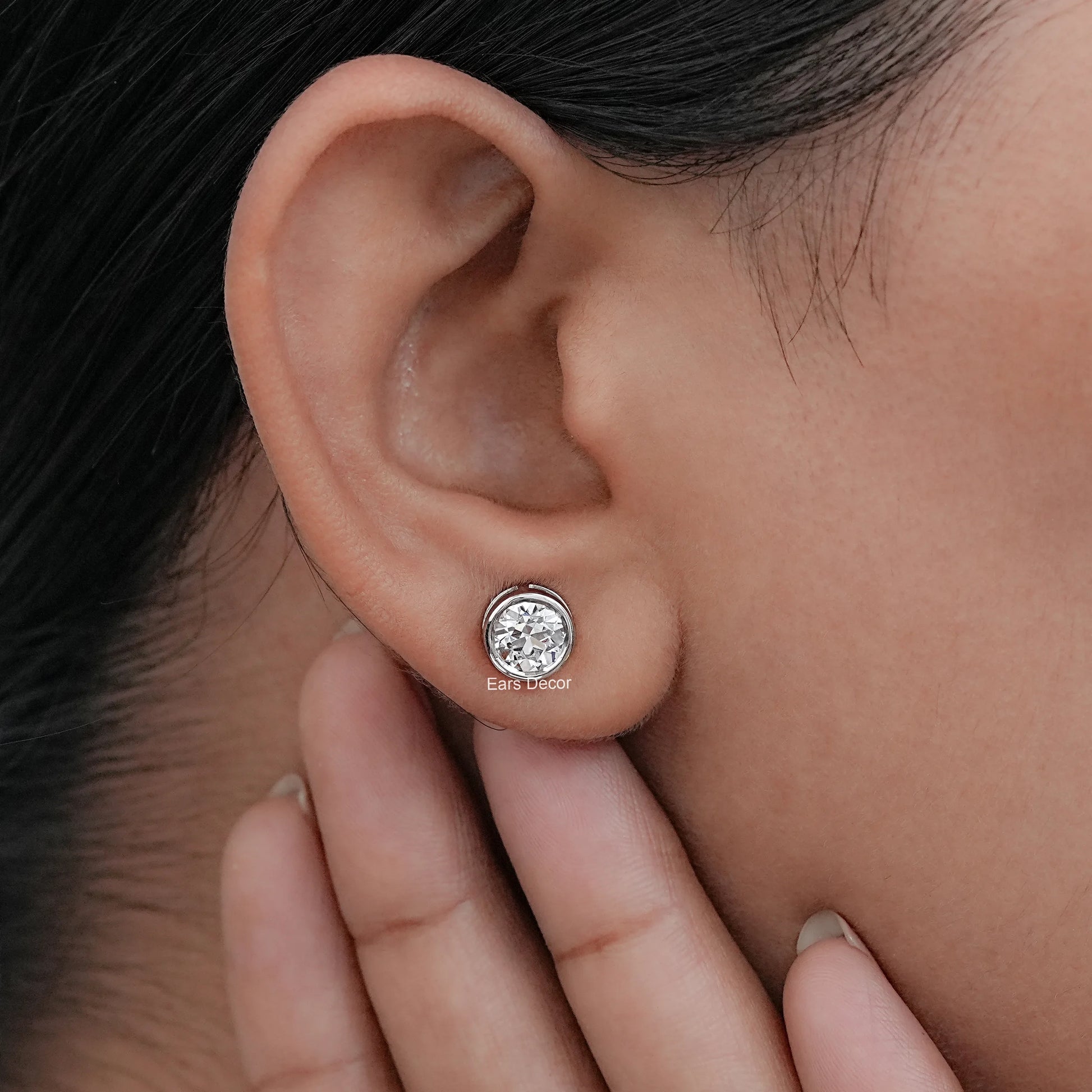 Old European round cut lab diamond bezel set stud earrings worn in an ear, showcasing elegance and craftsmanship.
