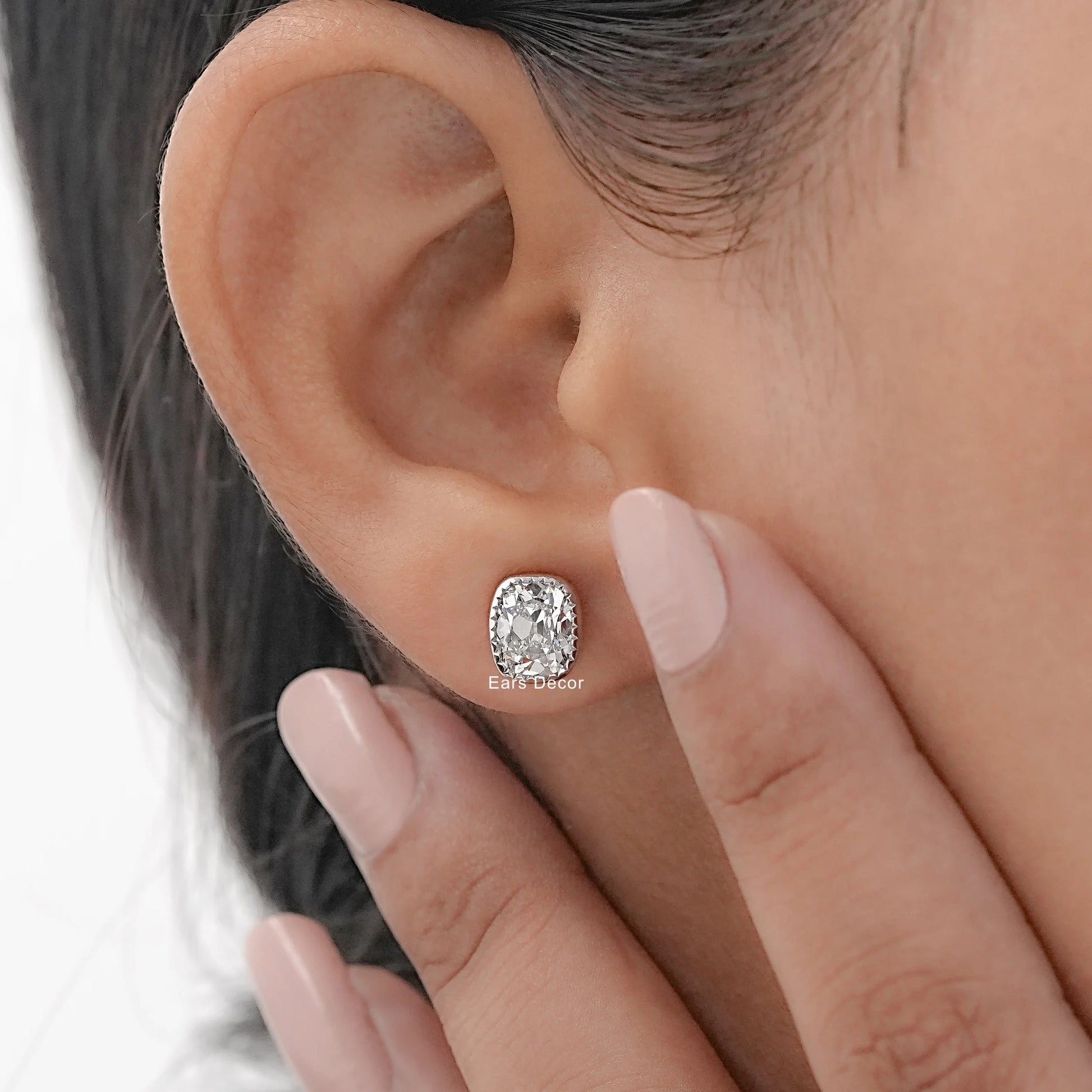 Halo cushion cut diamond stud earrings white gold milgrain bezel worn model ear hand touching dark hair nude manicure warm skin