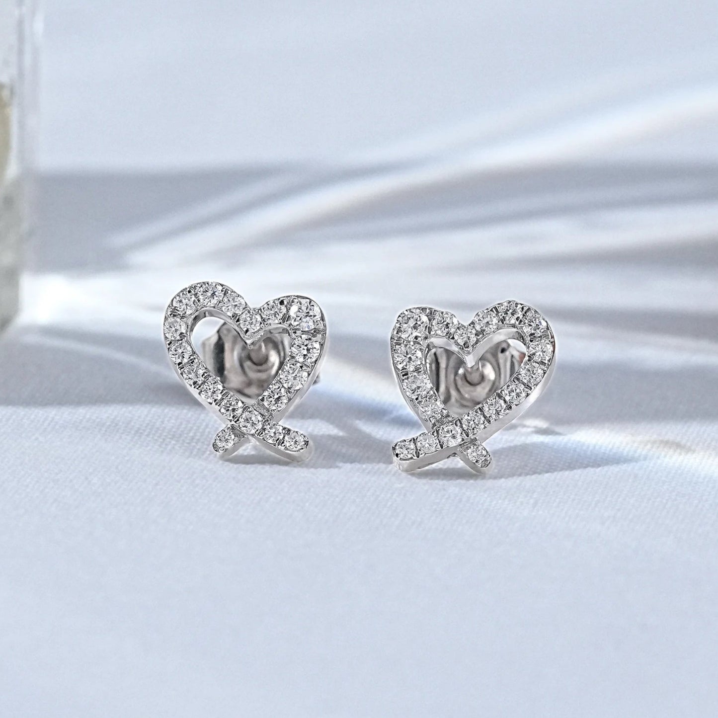 Dainty white gold heart shaped pavé diamond stud earrings displayed on a clean white surface with soft shadows.